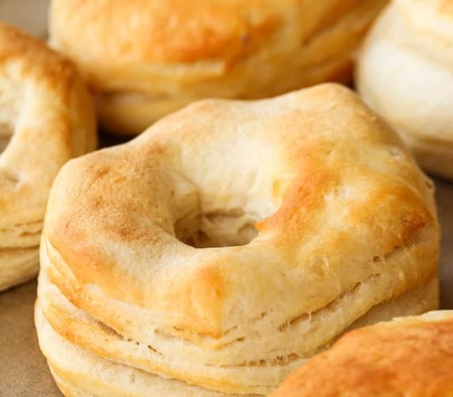 A warm donut being dipped in melted butter and rolled through cinnamon sugar