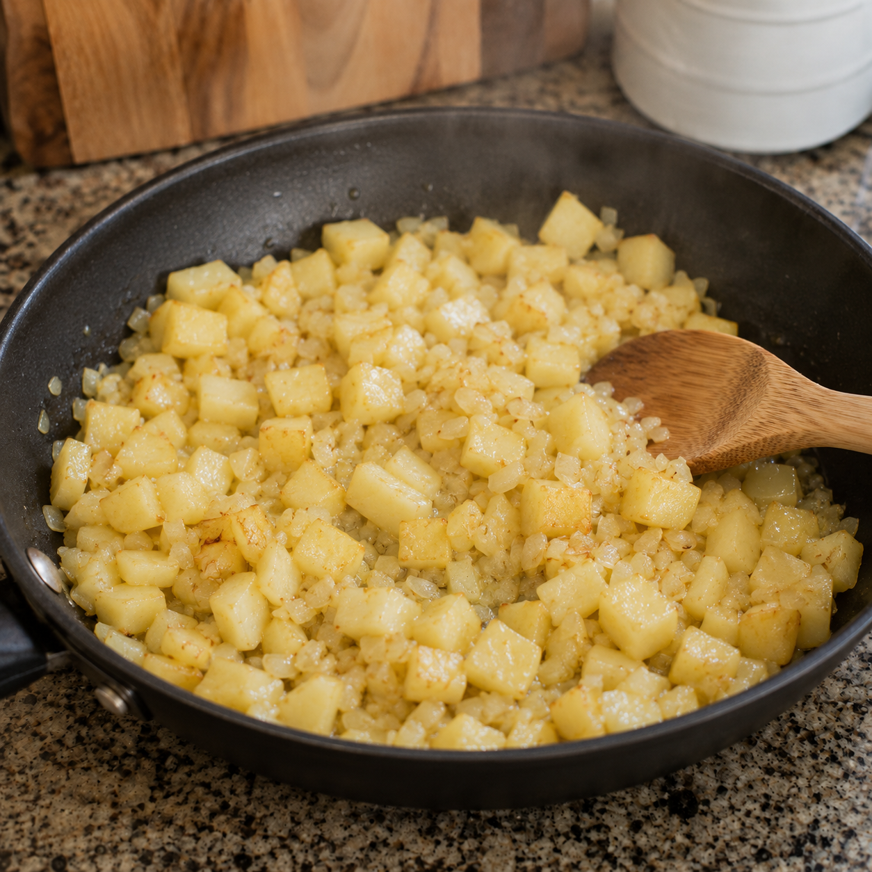 Steamed potato cubes and diced onion in a pan with butter